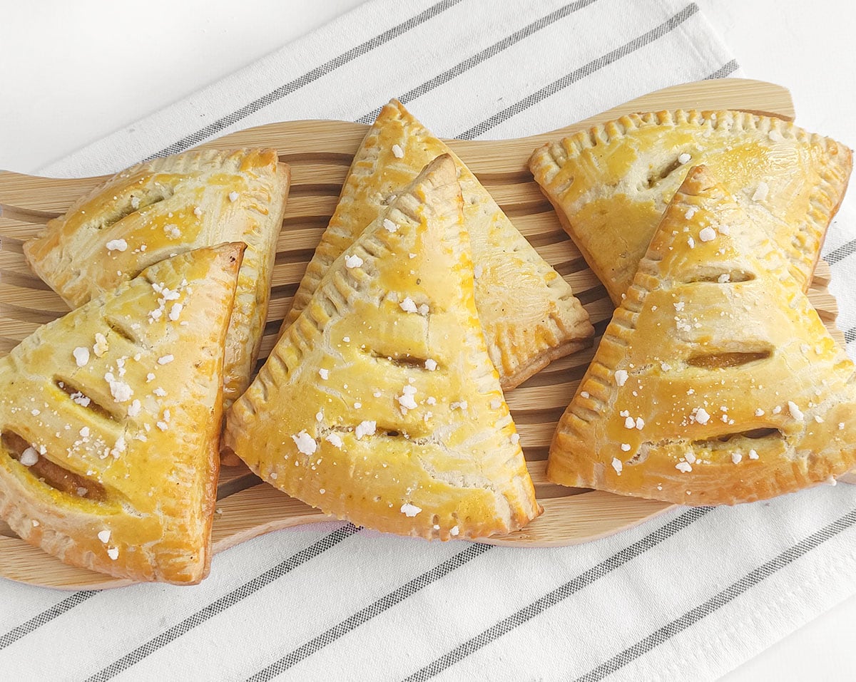 Golden brown pastry turnovers with vented tops resting on a wooden serving board