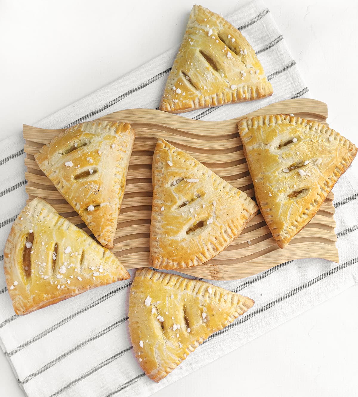 Top-down view of golden baked triangular turnovers sprinkled with coarse sugar on a wooden board